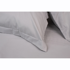Jogo de lençol solteiro em percal 100% algodão na cor cinza, com travesseiros sobre a cama.