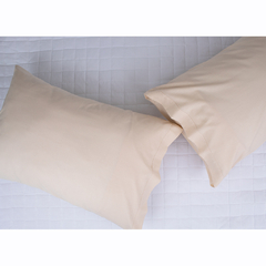 Fronhas de percal 100% algodão na cor bege, dispostas sobre uma cama com colcha branca.