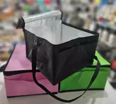 Lonchera térmica de tela de 4 litros, color negro, con interior aislante, sobre cajas de colores rosa y verde.