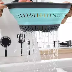 Colador plegable redondo en uso, drenando agua de frutas o verduras.