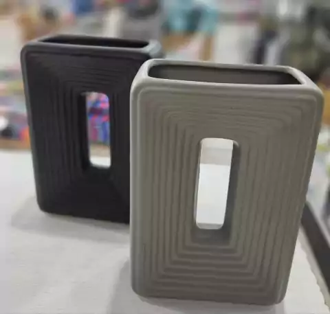 Florero rectangular de cerámica en colores gris y negro con diseño estriado y hueco central.