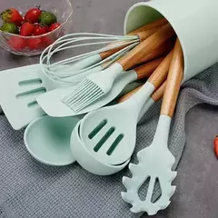 Conjunto de utensilios de cocina de silicona verde y madera, incluyendo espátula, cuchara y batidor, presentados en un recipiente.