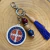 Chaveiro com medalha de São Bento, conta com detalhes artesanais em contas coloridas e tassel azul, sobre superfície de madeira