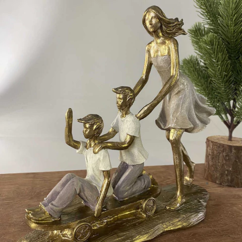 Escultura decorativa de mãe empurrando dois meninos brincando em carrinho de madeira, em tons dourados e brancos