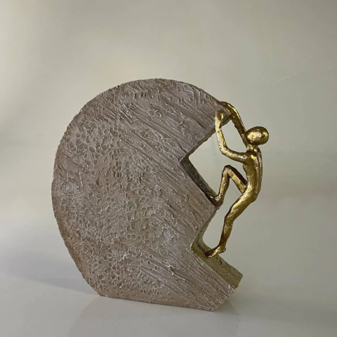 Escultura decorativa contemporânea de superação com figura dourada subindo uma parede texturizada cinza de 19 cm