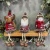 Guirlanda de Natal com bonecos decorativos de rena, Papai Noel e boneco de neve sentados em uma prateleira de madeira, todos com roupas vermelhas e detalhes em pele falsa