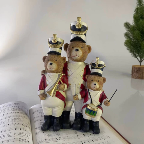 Trio de ursinhos decorativos vestidos como banda de música, com 22 cm, em uniforme vermelho, branco e dourado, posicionados sobre uma partitura musical.