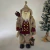 Papai Noel realista vestido com casaco bege e marsala segurando lanterna e saco de presentes, ao lado de árvore de Natal decorada