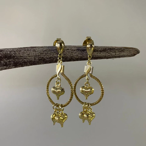 Brincos de capim dourado com pingentes em formato de coração dourados pendurados em aro circular