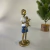 Escultura decorativa de menino dourado segurando um gato, vestindo camiseta branca e shorts azuis, com altura de 16 cm