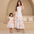 Conjunto Tal Mãe Tal Filha com vestidos brancos florais, modelo adulto usando vestido mídi e criança com vestido curto, ambos com estampa floral colorida