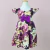 Vestido infantil Helena floral uva com estampa de flores grandes em tons de roxo, amarelo e branco, com laço roxo no centro e mangas curtas franzidas