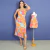 Mulher vestindo vestido midi tal mãe tal filha com estampa floral laranja e rosa, ao lado de vestido infantil igual em manequim