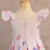 Vestido infantil rosa claro com estampa de borboletas em tons de rosa e lilás, com mangas bufantes e fecho de zíper nas costas