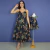 Mulher usando vestido midi preto com estampa de folhas coloridas ao lado de vestido infantil com mesma estampa em manequim