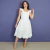Mulher usando vestido midi branco off white com alças largas e babados, posando em fundo azul