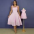 Mulher usando vestido rosa bebê mídi com alças e detalhes de babado, ao lado de vestido infantil rosa bebê similar em manequim