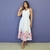 Mulher vestindo vestido midi branco com estampa floral colorida na barra, posando em fundo roxo