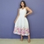 Vestido midi branco com estampa floral colorida na barra, modelo Jessica, usado por mulher em fundo roxo