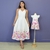 Vestidos tal mãe tal filha Jessica e Mônaco Jardim em tecido branco com estampa floral colorida na barra, modelo midi para mãe e vestido infantil com laço rosa na cintura em manequim