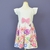 Vestido infantil branco com estampa florida colorida, laço rosa na cintura e mangas curtas com babado