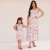 Mulher e menina usando vestidos midi floridos combinando em branco com estampas vermelhas e rosa, posando de mãos dadas em fundo claro
