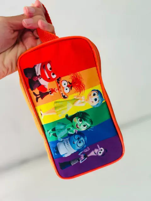 Porta lápis colorido com personagens de animação em fundo arco-íris, segurado por uma mão.