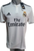 Camiseta blanca del Real Madrid, modelo profesional de fútbol, con el logo de Adidas y el escudo del club.