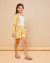 Menina vestindo conjunto infantil feminino com jaqueta e shorts amarelos estampados com margaridas, camiseta branca e sandálias transparentes