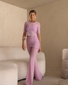 Mulher usando um conjunto rosa claro com blusa de tule e calça flare, posando em um ambiente moderno.