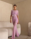 Mulher usando um conjunto rosa claro com blusa de tule e calça flare, posando em um ambiente moderno.