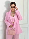 Modelo usando um conjunto de blazer cropped e calça rosa, com acessórios de pérolas e bolsa de palha.