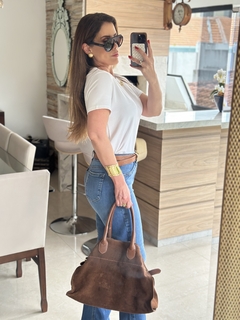 Modelo usando uma blusa branca básica de algodão com calça jeans, segurando uma bolsa marrom em um ambiente moderno.