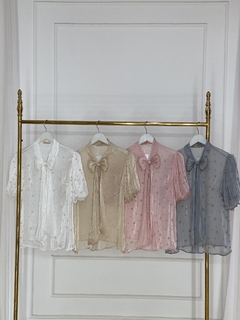 Quatro camisas perola gola com amarração em diferentes cores penduradas em um cabideiro dourado.