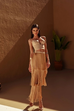Modelo usando blusa cropped Debbie em tom claro, combinada com saia longa de franjas em um ambiente iluminado.