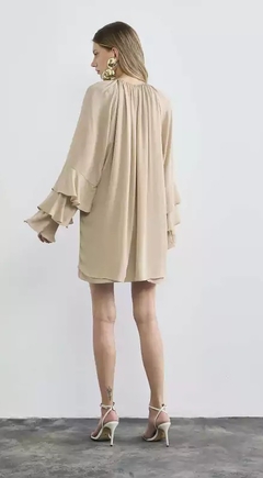 Modelo usando um vestido curto plissado Agnes, com mangas largas e detalhe de babados, na cor bege.
