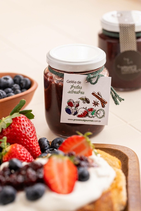 Potinho de geleia de frutas vermelhas da Provençal Gourmet com etiqueta ilustrativa ao lado de frutas frescas e torrada com creme e frutas