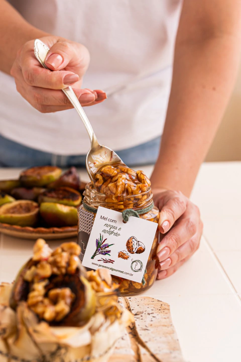 Pessoa segurando pote de mel com açafrão e nozes da Provençal Gourmet e  retirando uma colherada do produto.