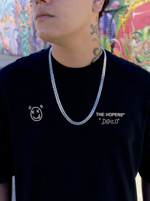 Jovem usando uma corrente DUPLO GRUMET 8mm em prata 925, posando em frente a um mural colorido.