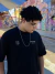 Jovem usando uma camiseta preta e óculos, com uma corrente prata 925 pendurada no pescoço, em um ambiente urbano colorido.