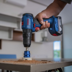 Taladro de percusión a batería Bosch GSB 18V-50 en uso, perforando una superficie con polvo alrededor.