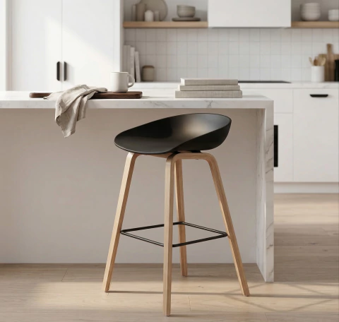 Banqueta nórdica negra con asiento de polipropileno y patas metálicas simil madera, ubicada en una cocina moderna junto a una barra desayunadora.