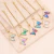 Pulseras doradas con dijes de mariposas de cristal tornasol en diferentes colores sobre una base de piedra clara