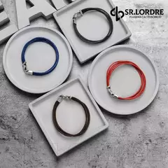 Pulseiras masculinas de couro genuíno em diferentes cores, apresentadas em pratos brancos sobre uma superfície cinza.