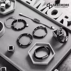 Conjunto de pulseiras masculinas em couro e aço inox, incluindo modelos com caveira, dispostas sobre uma superfície cinza.