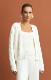 Modelo usando um casaco ambicione por anselmi off white com textura de ponto tijolinho, combinado com uma blusa e calça brancas.