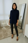 Mulher usando uma blusa ambicione por anselmi azul marinho com gola boba alta, combinada com calças pretas e sapatos de salto, em um ambiente moderno e iluminado.
