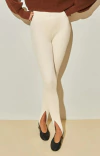 Calça feminina canelada Ambicione Por Anselmi na cor cru com detalhe em recortes na parte inferior, combinada com uma blusa marrom.