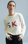 Modelo usando uma blusa ambicione por anselmi off white com a palavra "SKI" em destaque.