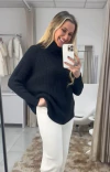 Mulher sorrindo enquanto usa uma blusa preta de gola alta ambicione por anselmi